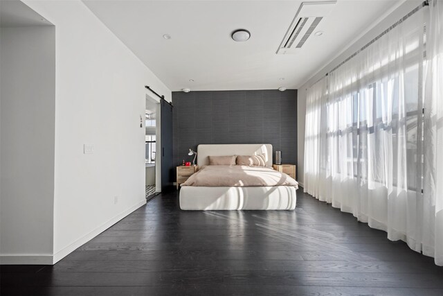 bedroom with an accent wall, a barn door, baseboards, and dark wood-type flooring