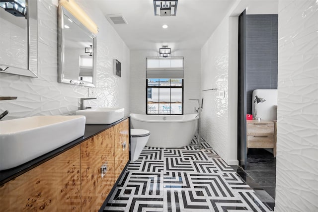 bathroom featuring visible vents, double vanity, a freestanding tub, tile patterned floors, and a sink