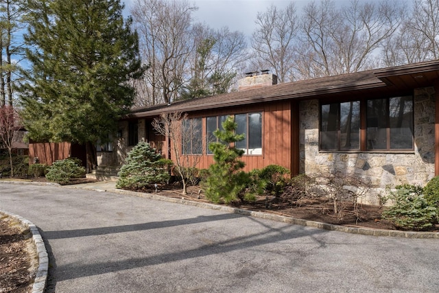 view of front of house featuring stone siding, a chimney, and fence