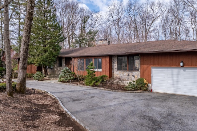 ranch-style home featuring a garage, stone siding, a chimney, and driveway