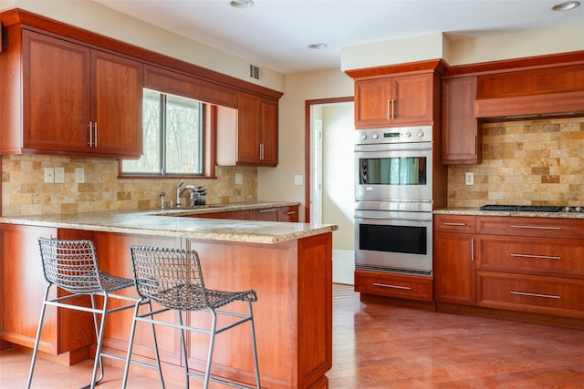 kitchen with brown cabinetry, a breakfast bar, a sink, appliances with stainless steel finishes, and light wood-type flooring