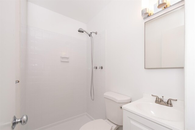 full bathroom with toilet, tiled shower, and vanity