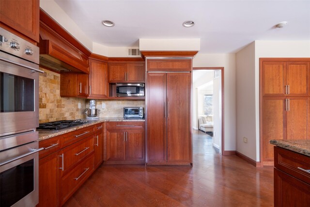 kitchen with visible vents, backsplash, light stone counters, appliances with stainless steel finishes, and dark wood-style flooring