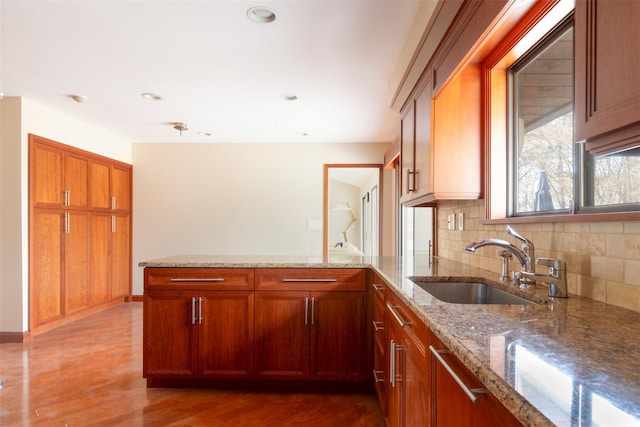 kitchen featuring light stone countertops, a peninsula, light wood-style flooring, a sink, and decorative backsplash