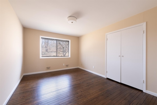 unfurnished bedroom featuring visible vents, baseboards, a closet, and dark wood-style flooring