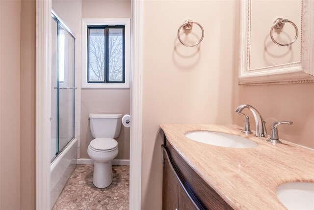 full bath featuring baseboards, toilet, double vanity, shower / bath combination with glass door, and a sink