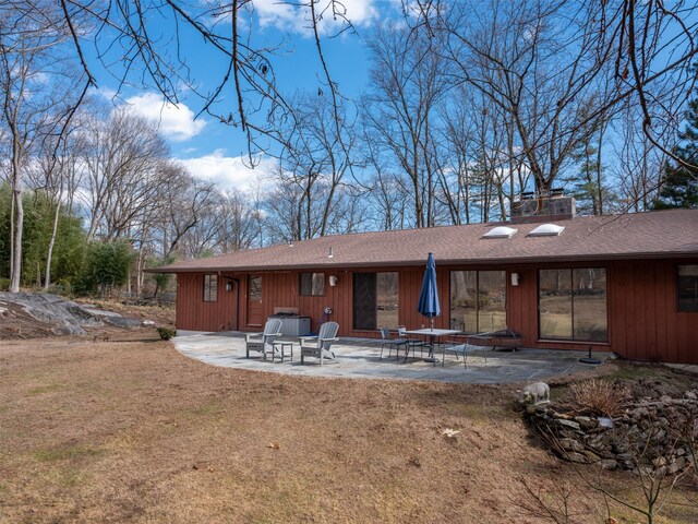 back of house with a patio, a yard, roof with shingles, and a chimney