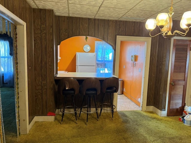 carpeted dining area with a chandelier, wooden walls, a dry bar, and baseboards