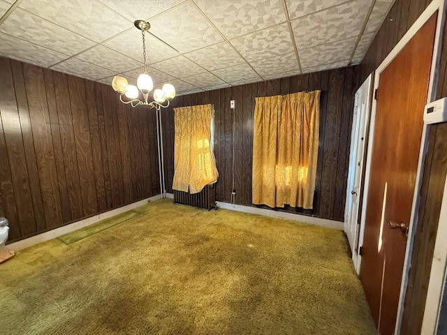 carpeted empty room featuring a notable chandelier, wood walls, and baseboards