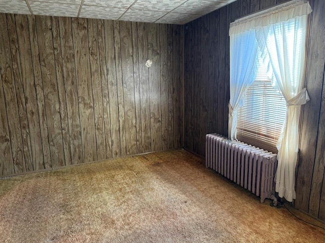 carpeted spare room with radiator and wood walls