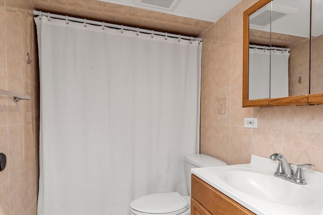 full bath with visible vents, toilet, tile walls, and vanity