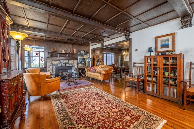 living room with a stone fireplace, a healthy amount of sunlight, coffered ceiling, and hardwood / wood-style flooring