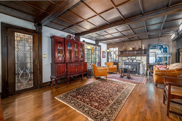 living area featuring coffered ceiling, a stone fireplace, and hardwood / wood-style floors