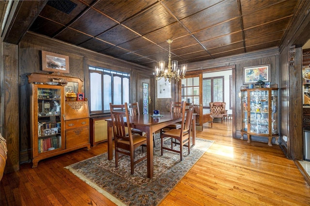 dining space with ornamental molding, hardwood / wood-style flooring, wood walls, wooden ceiling, and a chandelier