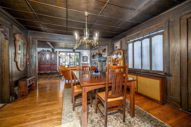 dining room with a chandelier, wood walls, coffered ceiling, and hardwood / wood-style floors