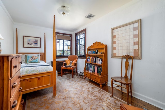 bedroom featuring visible vents, crown molding, baseboards, and wood finished floors