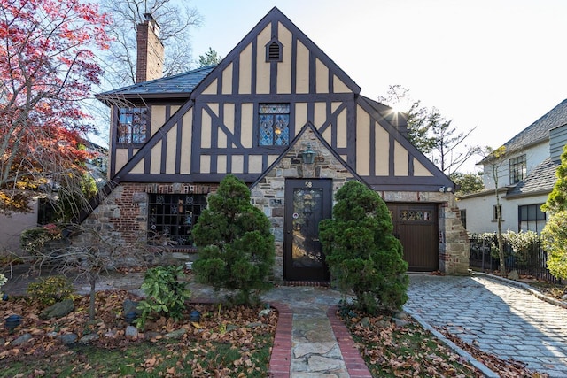 english style home with stucco siding, decorative driveway, stone siding, and a chimney