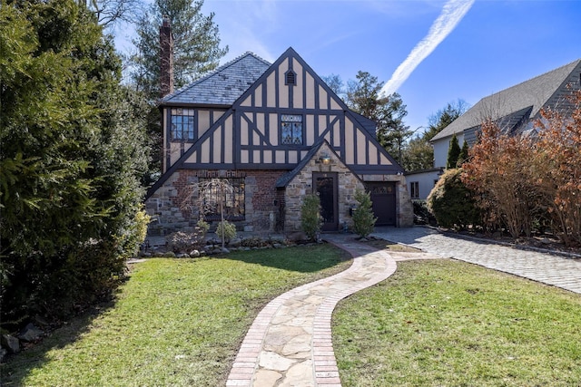 tudor house featuring stucco siding, decorative driveway, a front yard, a garage, and a chimney