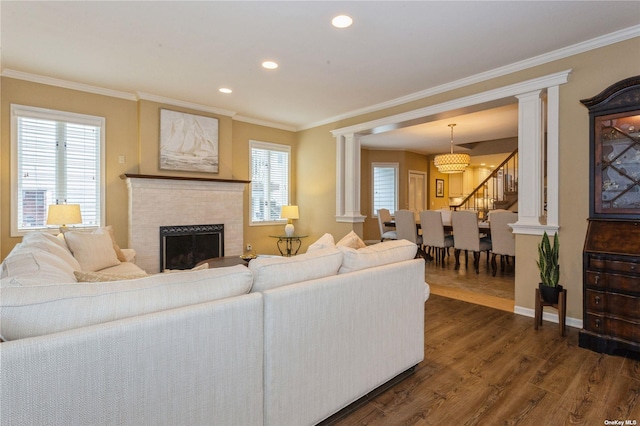 living room featuring crown molding, a brick fireplace, decorative columns, and dark wood-style floors