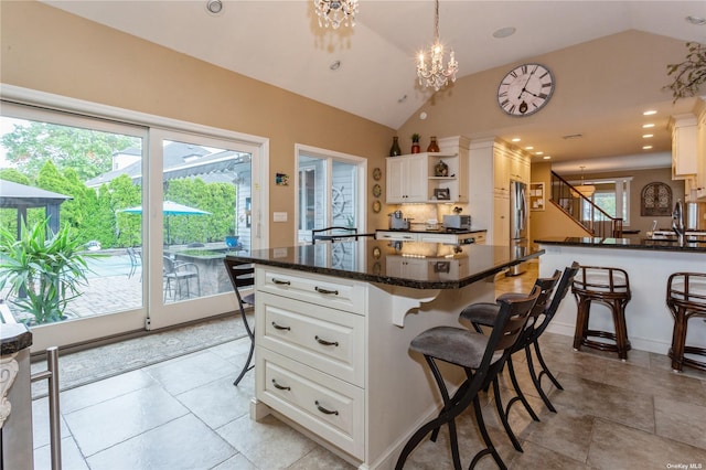 kitchen with open shelves, vaulted ceiling, white cabinets, a kitchen breakfast bar, and a chandelier