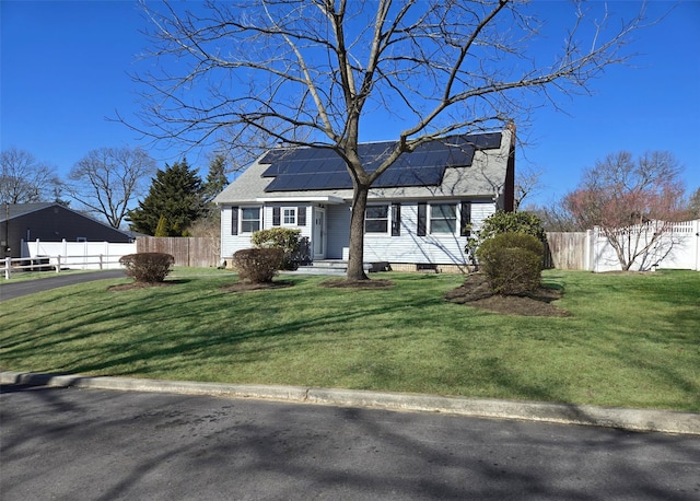 view of front of home featuring roof mounted solar panels, a shingled roof, a front lawn, and fence