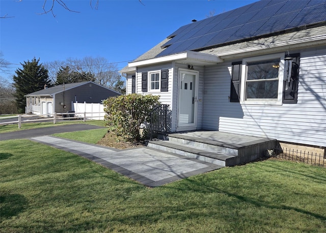 entrance to property with solar panels, a shingled roof, a yard, and fence