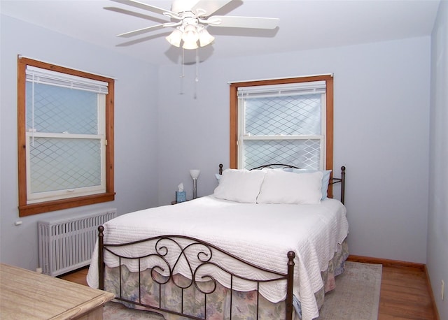 bedroom with a ceiling fan, radiator, wood finished floors, and baseboards