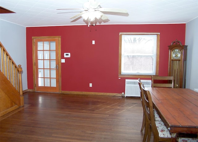 unfurnished dining area featuring radiator, baseboards, stairs, wood finished floors, and a ceiling fan