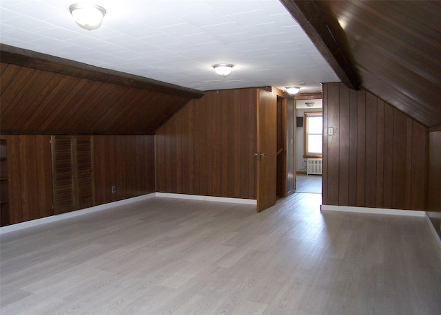 additional living space featuring light wood-style flooring, lofted ceiling with beams, radiator heating unit, wood walls, and baseboards