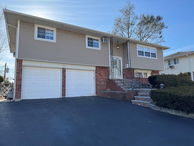 raised ranch featuring aphalt driveway, brick siding, a wall mounted AC, and a garage