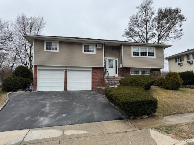 bi-level home with aphalt driveway, a garage, and brick siding