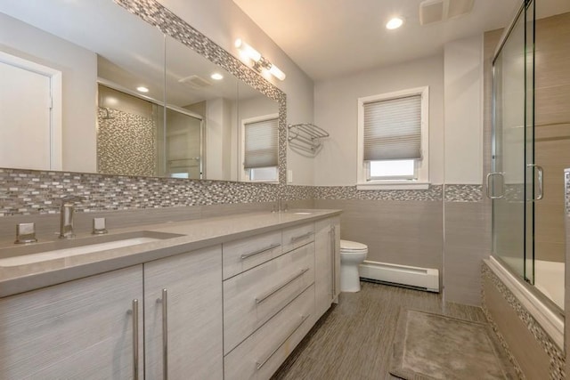 bathroom with a sink, a baseboard radiator, tiled shower, and visible vents