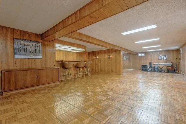 finished basement featuring wood walls, a dry bar, and a textured ceiling