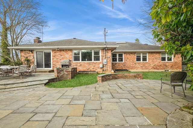 back of property featuring a shingled roof, a patio, brick siding, and a chimney