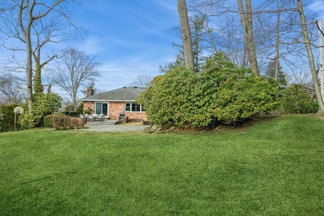 rear view of house featuring a yard, brick siding, a chimney, and a patio area