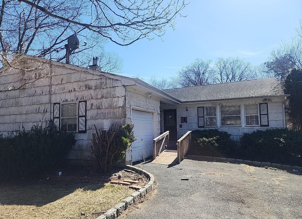 single story home with an attached garage, driveway, and roof with shingles