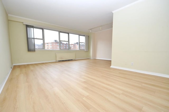 empty room with light wood-style flooring, radiator, baseboards, and ornamental molding