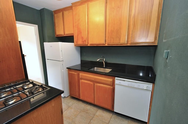 kitchen featuring white appliances, dark countertops, and a sink