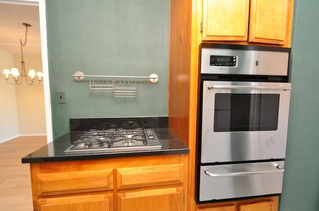 kitchen with a warming drawer, appliances with stainless steel finishes, wood finished floors, and an inviting chandelier