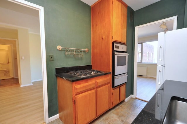 kitchen with wall oven, stainless steel gas cooktop, light wood-style flooring, freestanding refrigerator, and a warming drawer