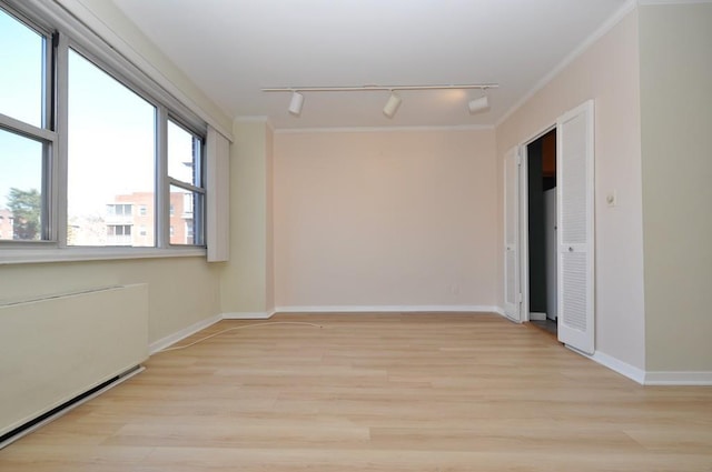 spare room featuring baseboards, light wood-type flooring, and ornamental molding