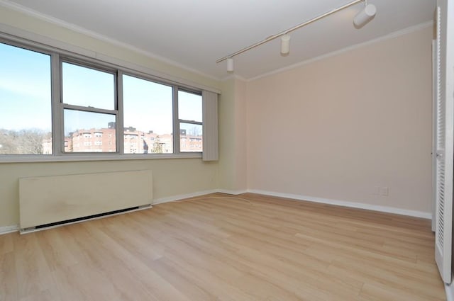 empty room featuring track lighting, light wood-style flooring, crown molding, and radiator heating unit