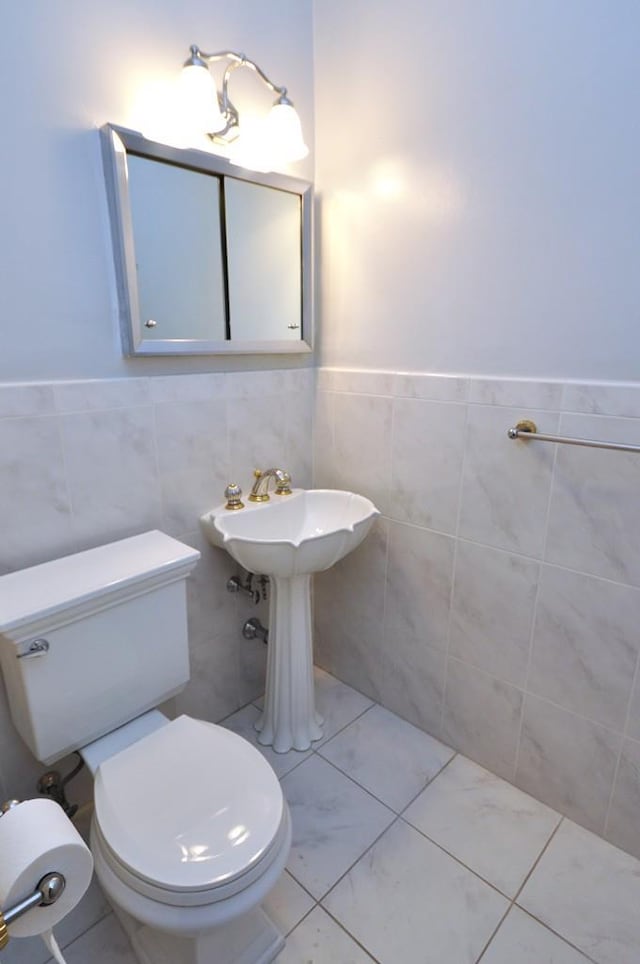 half bath featuring wainscoting, toilet, and tile walls