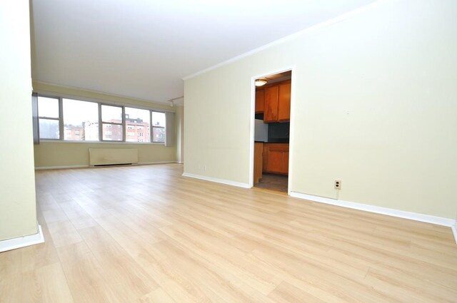 empty room with baseboards, crown molding, and light wood-style floors