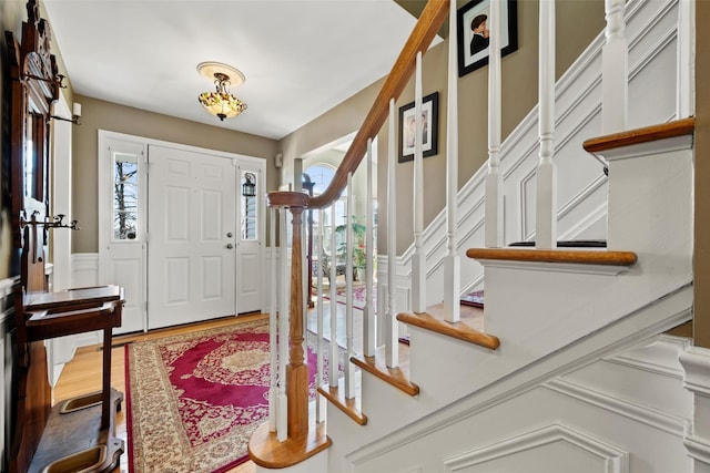 foyer with stairs, plenty of natural light, wood finished floors, and wainscoting