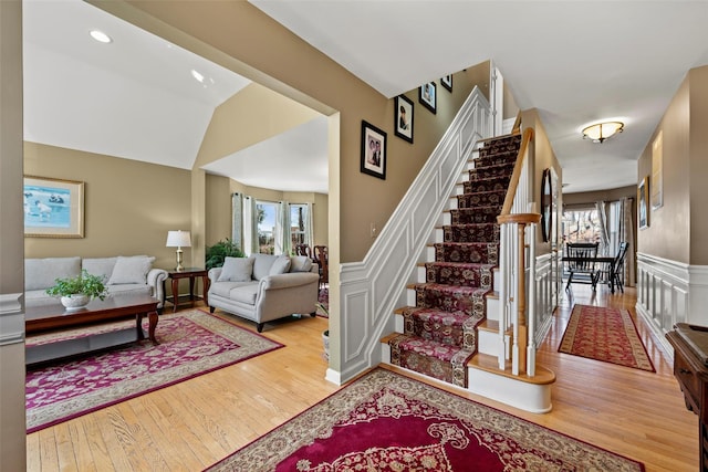 stairway with vaulted ceiling, a decorative wall, wainscoting, and wood finished floors