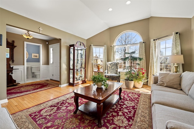 living area with vaulted ceiling, wood finished floors, and wainscoting