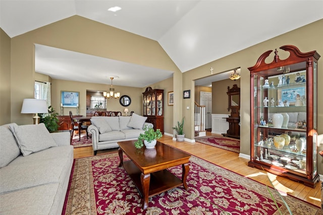 living room featuring stairs, vaulted ceiling, a notable chandelier, and wood finished floors