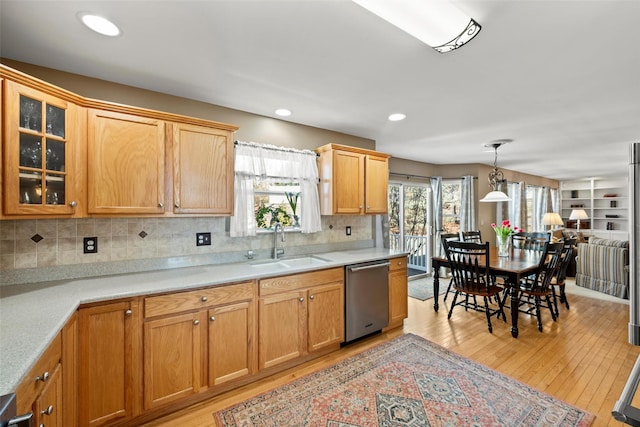 kitchen with light wood-style flooring, a sink, light countertops, glass insert cabinets, and dishwasher