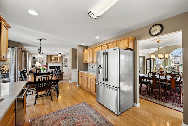 kitchen with light wood finished floors, light countertops, a fireplace, stainless steel refrigerator with ice dispenser, and hanging light fixtures